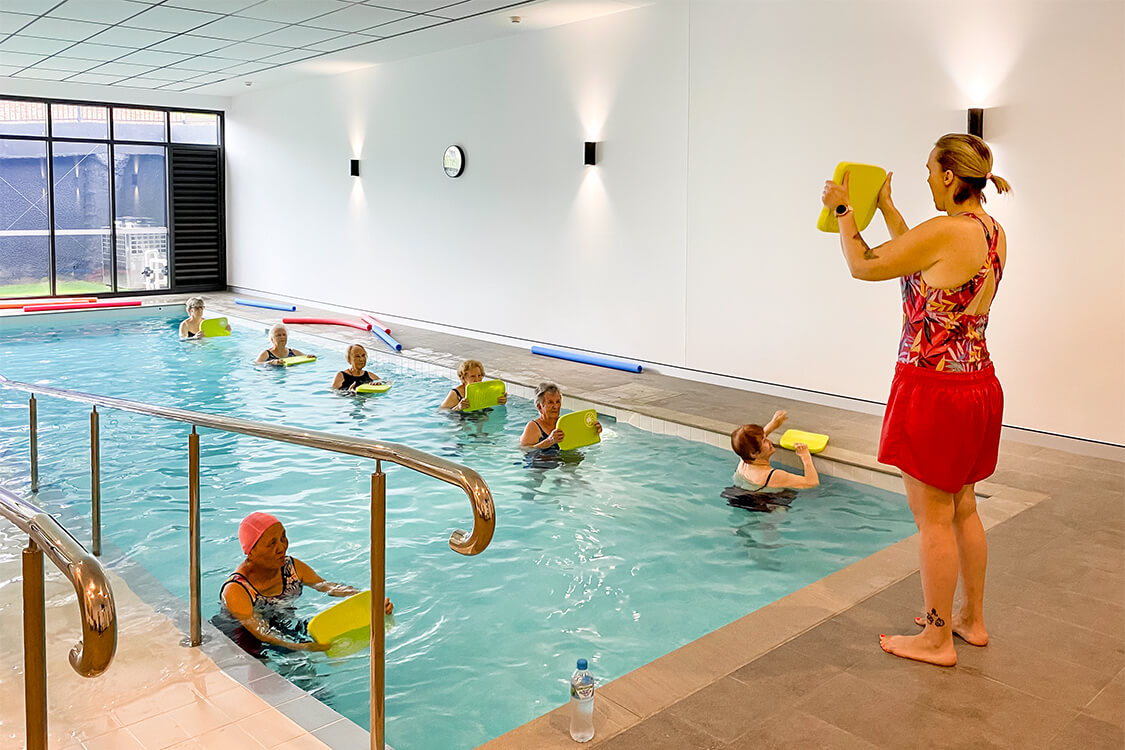 Physio holding a kickboard in front of a class in the pool.