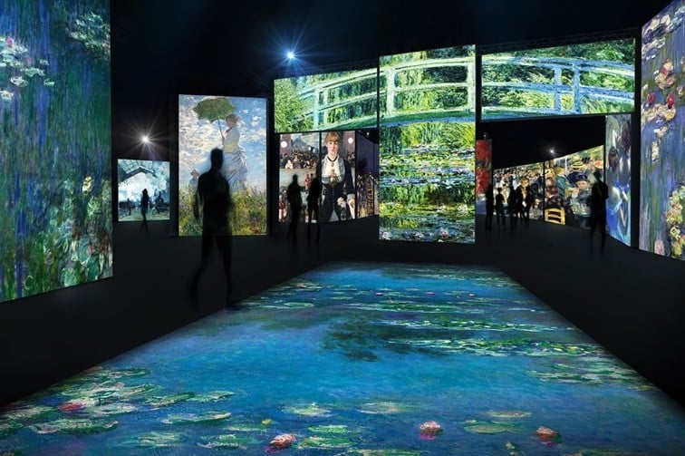 French impressionist art and Monet's waterlilies displayed on screens in a dark room, there is a shadow of a person walking passed.